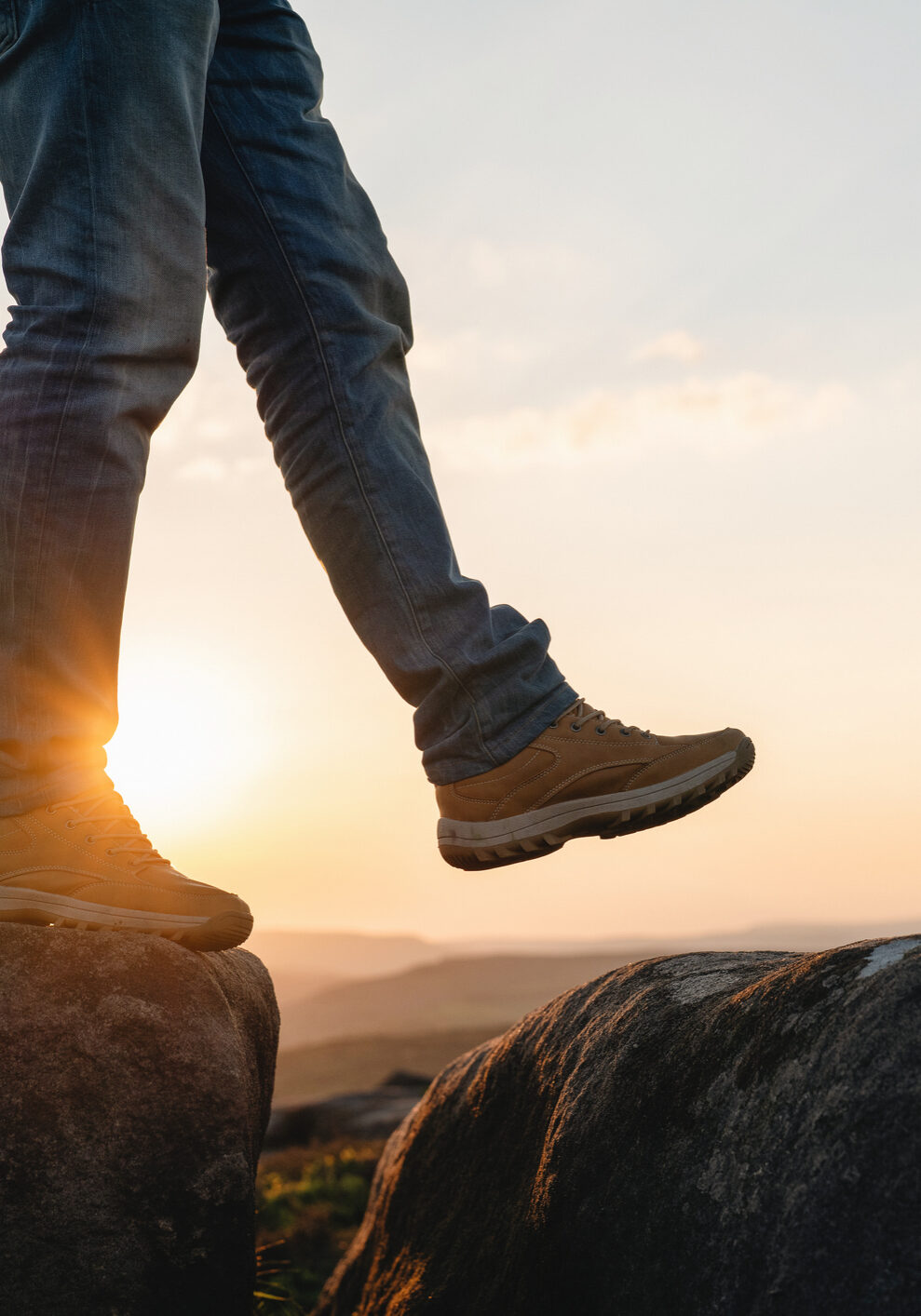 A person walks on large rocks while the sun sets in the background. The scene shows an outdoor environment during the evening, capturing a moment of exploration.